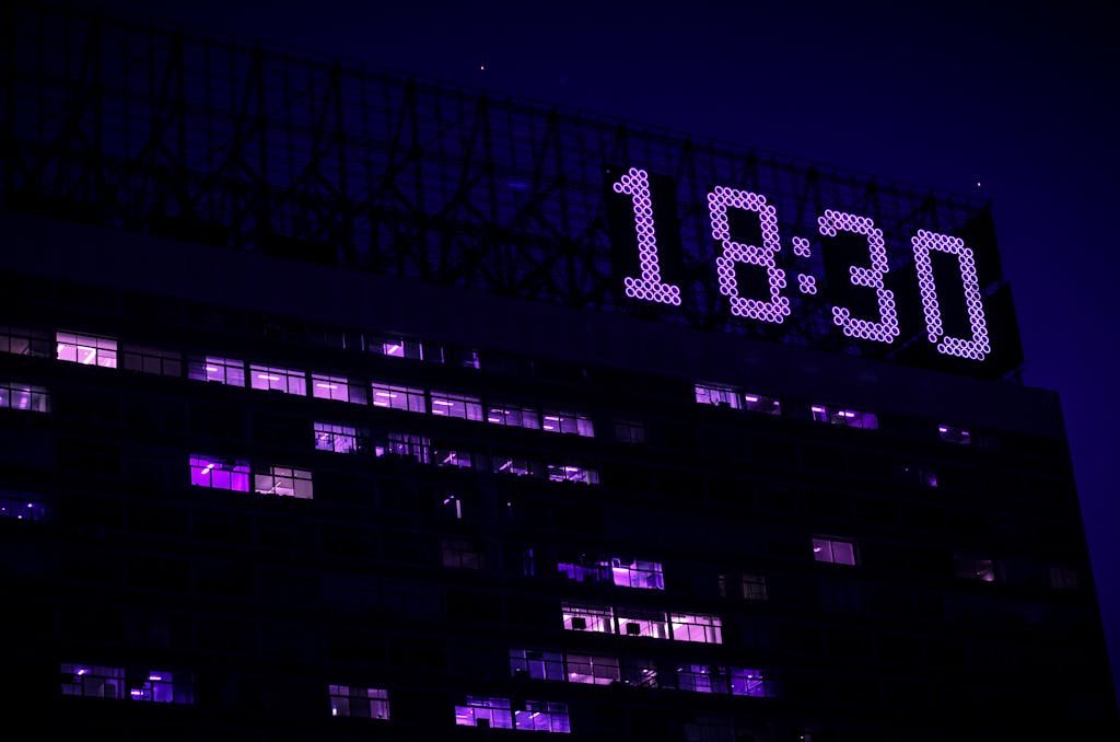 A modern building is illuminated at night with a prominent digital clock showing 18:30.